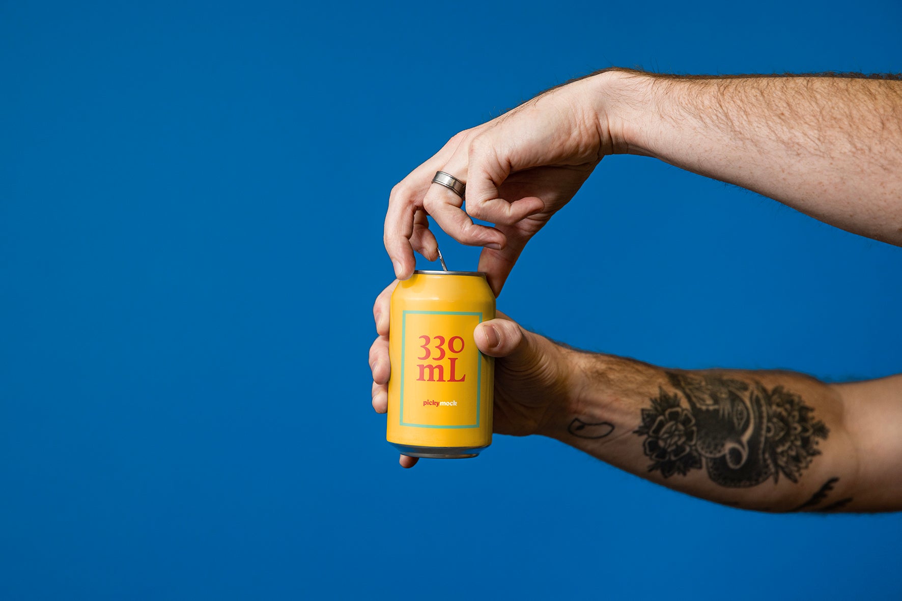 Bright drinks can is held up and opened by tattooed male arms, against a vibrant blue studio background. 