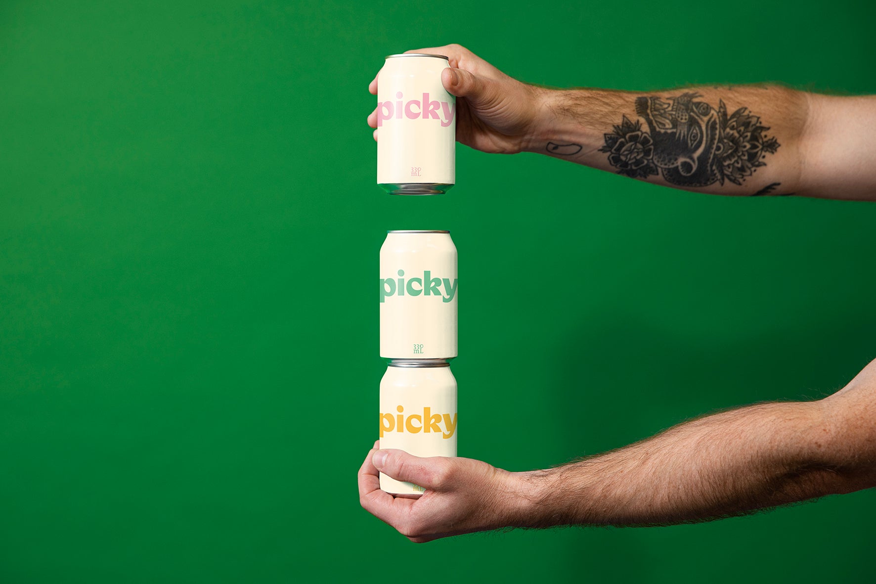 Tattooed arms hold out three cans stacked. Against a green studio backdrop.