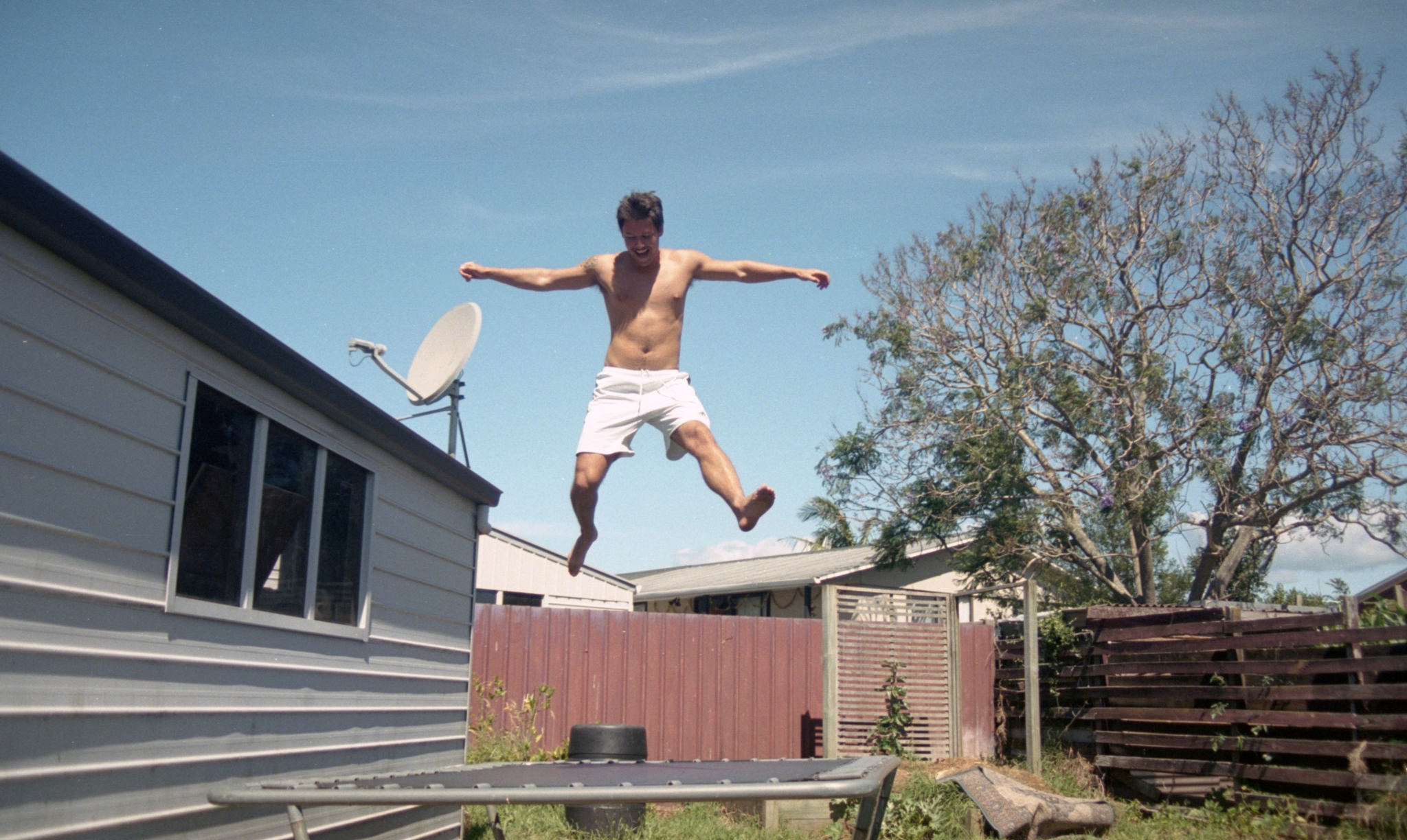 Young man jumps on trampoline on a bright blue day. 