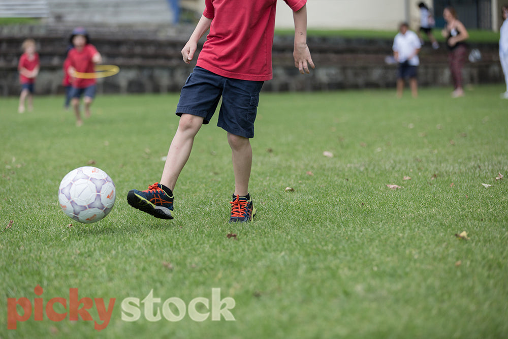 Child kicking a football in school uniform. 