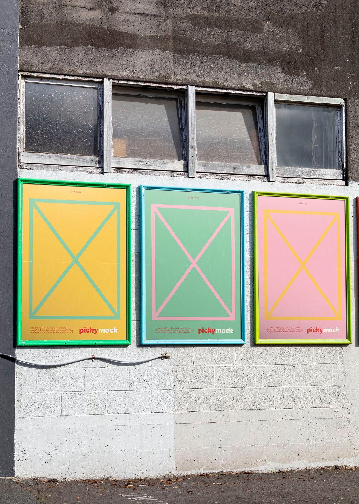 Three adshel billboards with bright borders on the side of an industrial white wall. Four windows above the street posters. 