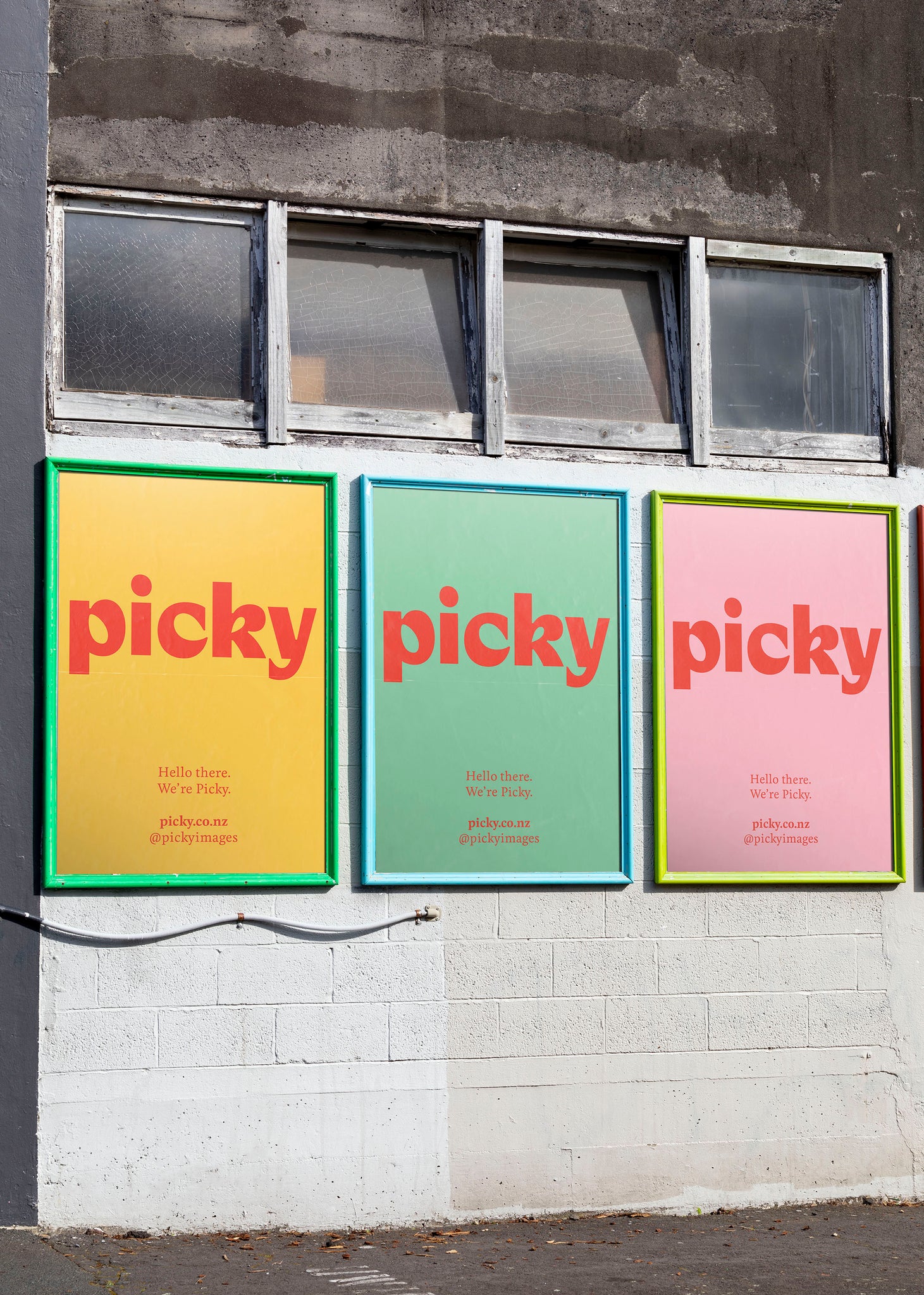 Three adshel billboards with bright borders on the side of an industrial white wall. Four windows above the street posters. Each Poster has the word Picky written in red against varying colours. 