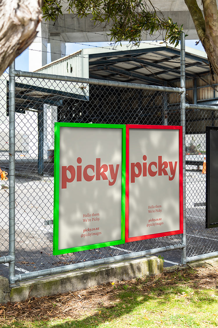 Portrait of colorful advertisement frames on a wire fence sheltered by trees, the frame holds white mock advertisement with a red picky logo.