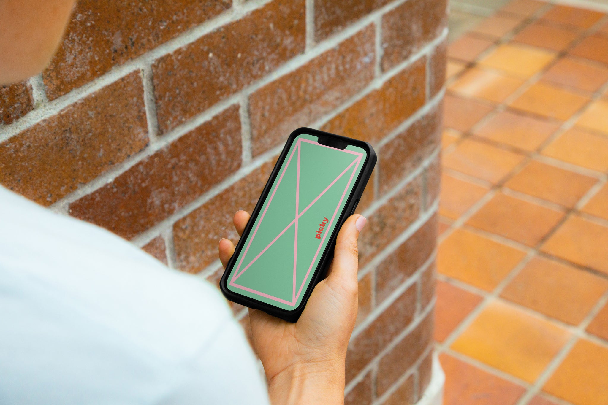 Lady holding smart phone standing against brick wall and path. Smartphone has screen turned on with green colour on sceen with pink grid lines visible.