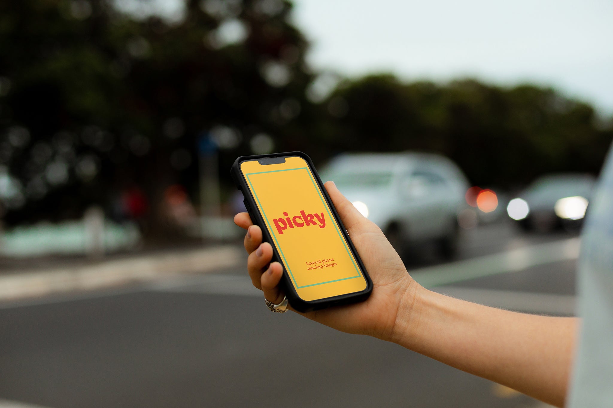 Man holding smart phone, iphone at traffic light crossing. Holding phone out, body cropped. Cars with headlights visible. Bright yellow screen with the words 'picky' written in red. 
