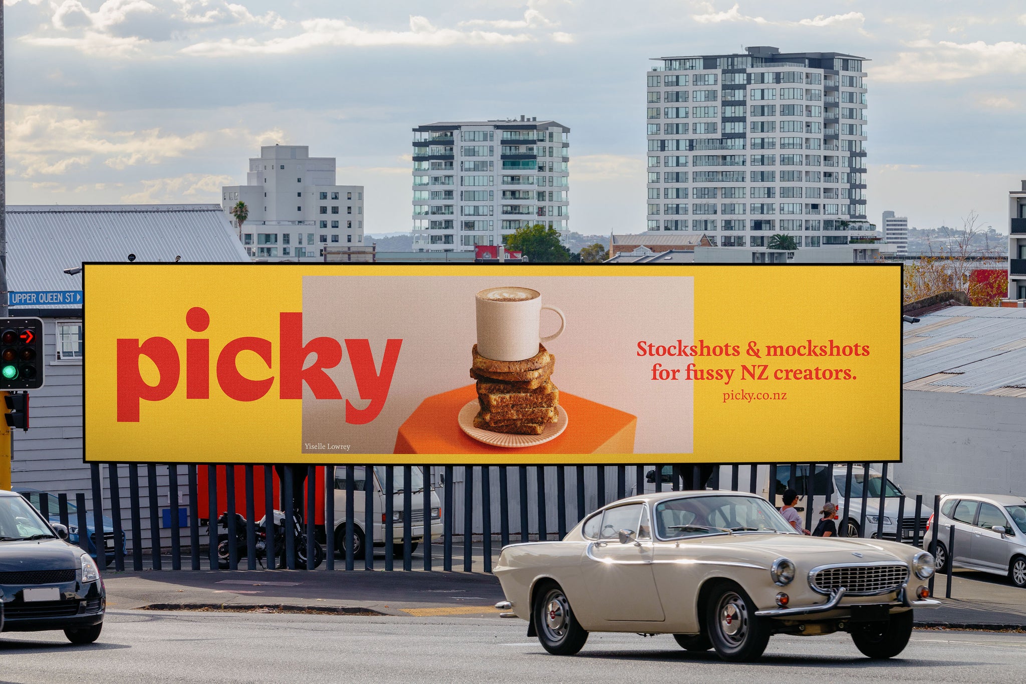 Mockup image of a long landscape billboard in Auckland city. With a beige vintage car in front of it.