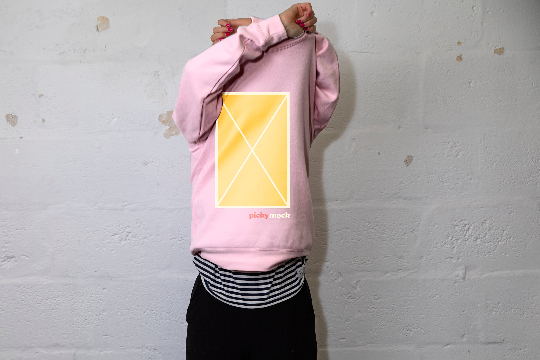 Person pulling a large pink jumper over their head with both hands above their head. A yellow box is in the middle of the jersey with white grid lines and an X in the middle. White cinderbock background. 