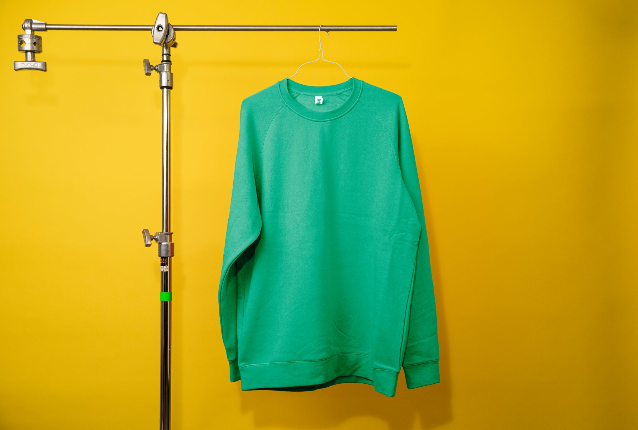 Photography c-stand holding a bright green jumper. Background is a bright yellow. 