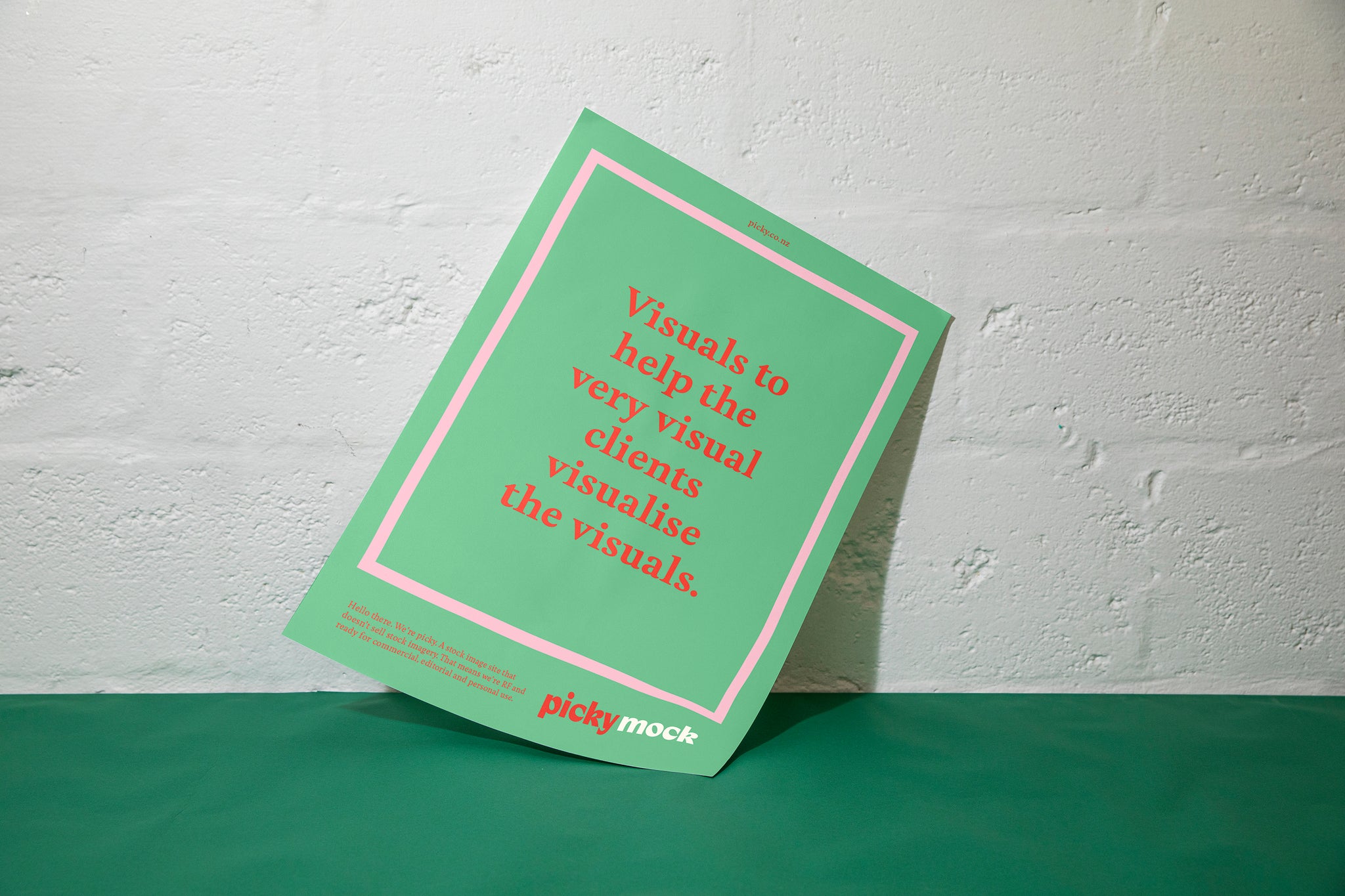 A green piece of card is sitting against a white cinder block wall and green surface. The card is green with a quote written in the middle of the frame. 