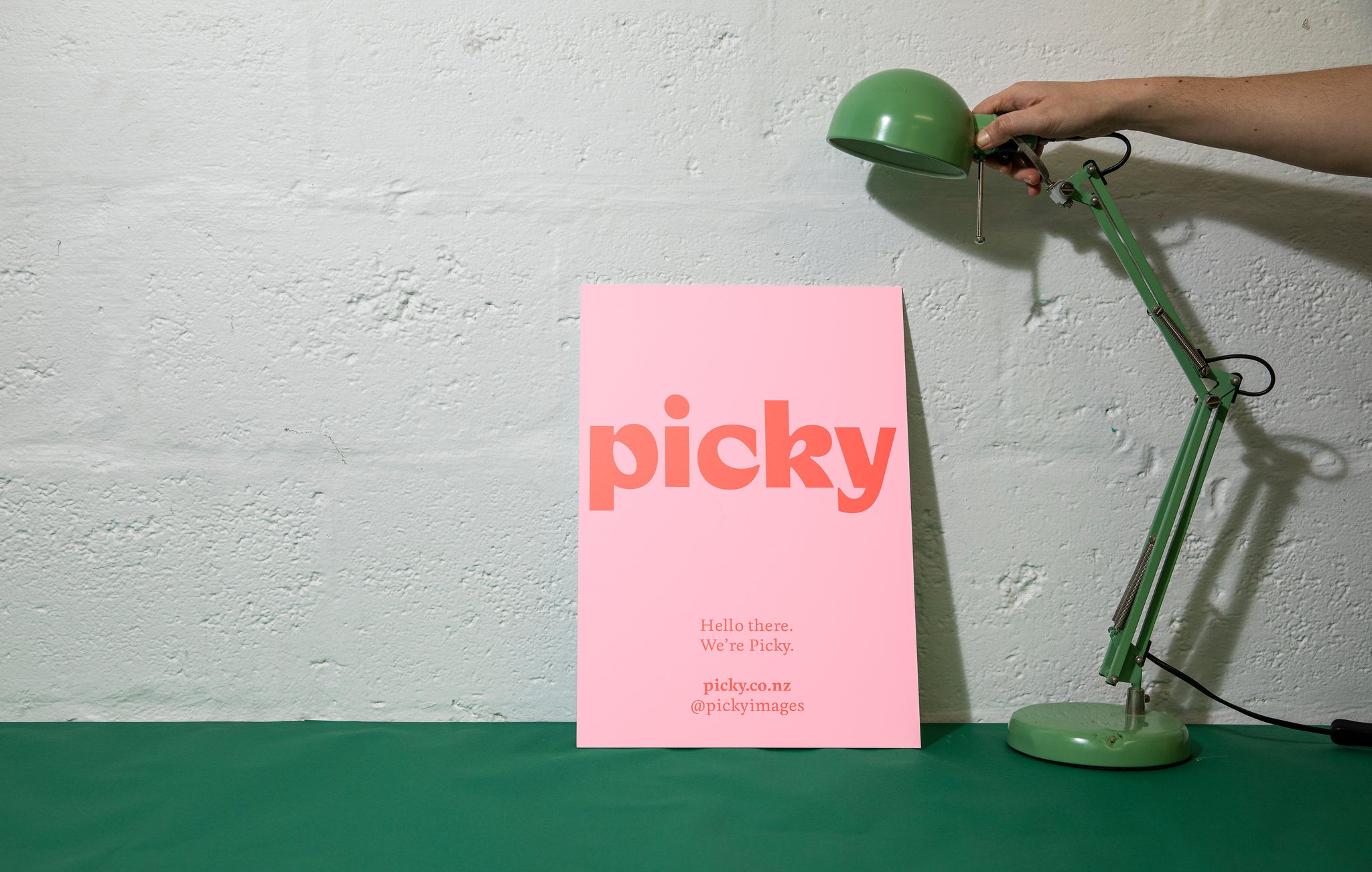 Landscape close-up of a hand holding a green lamp next to a large paper document in front of a white backdrop; it is pink with a large red mock-up advertisement.