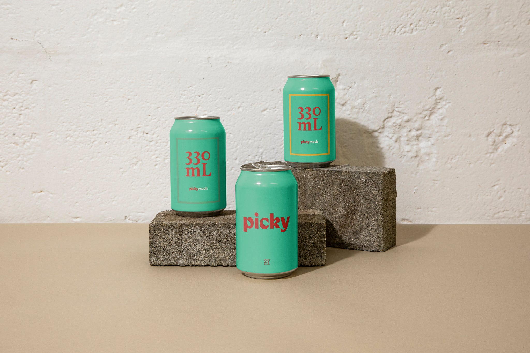 Landscape close-up of three 330ml cans posed atop grey bricks at different heights in front of a white brick wall; they are green with large white picky logo across the face.