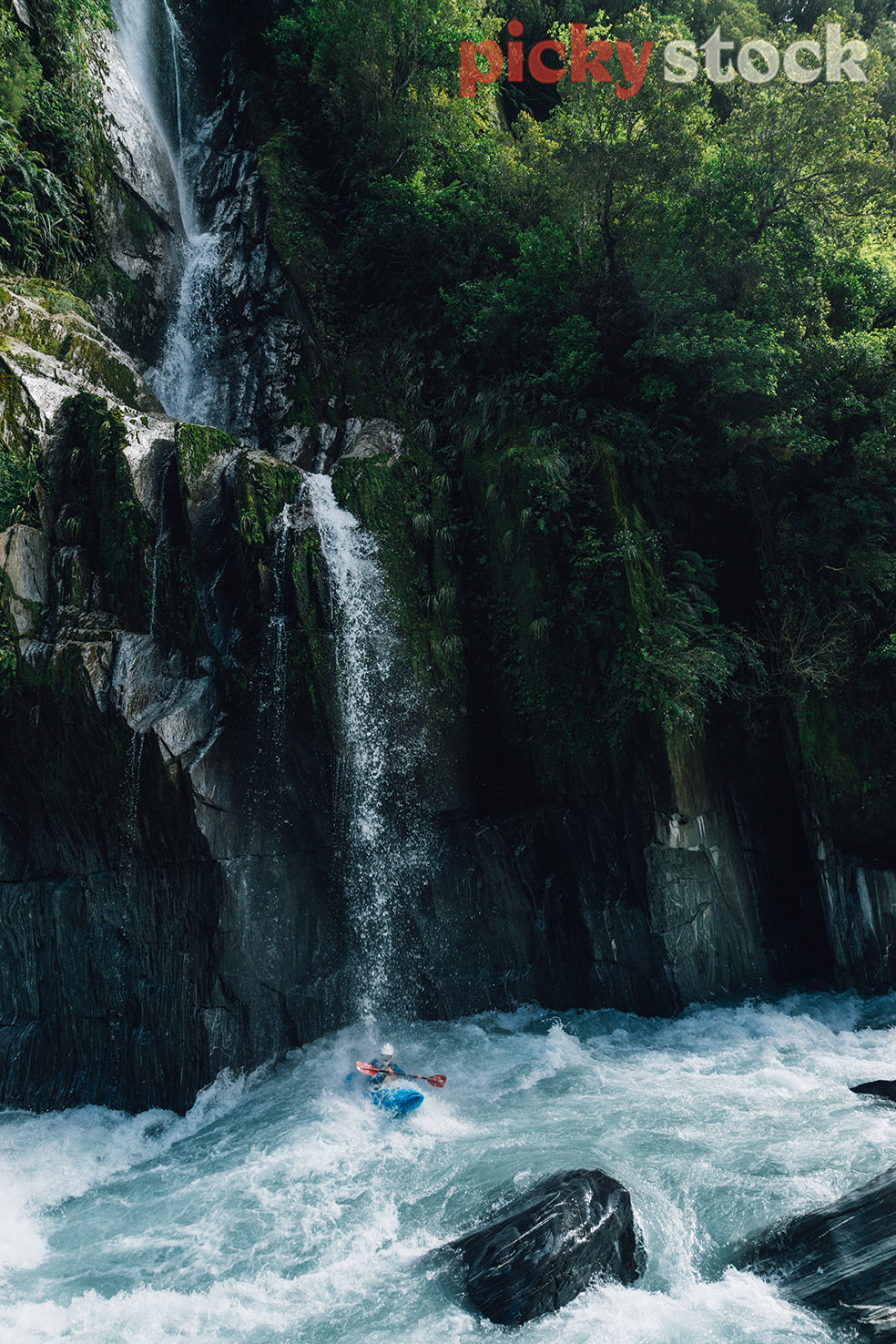 Whitewater kayaker paddling underneath a waterfall