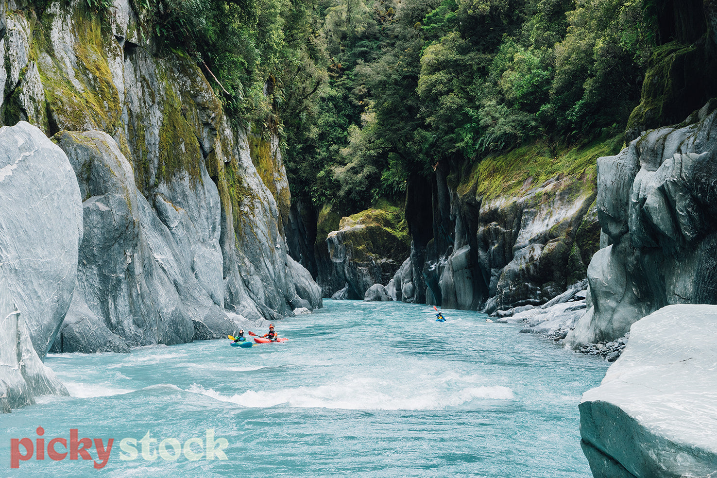 Three whitewater kayakers enjoying a beautiful river gorge on a glacial river