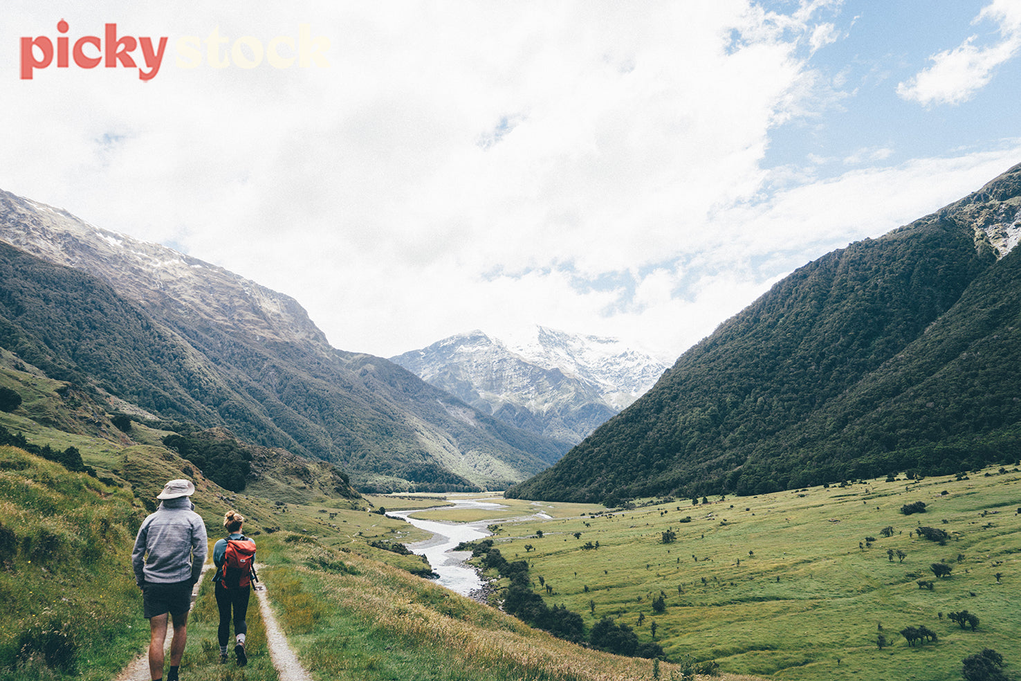 Two hikers walking in a valley next to the Matukituki River