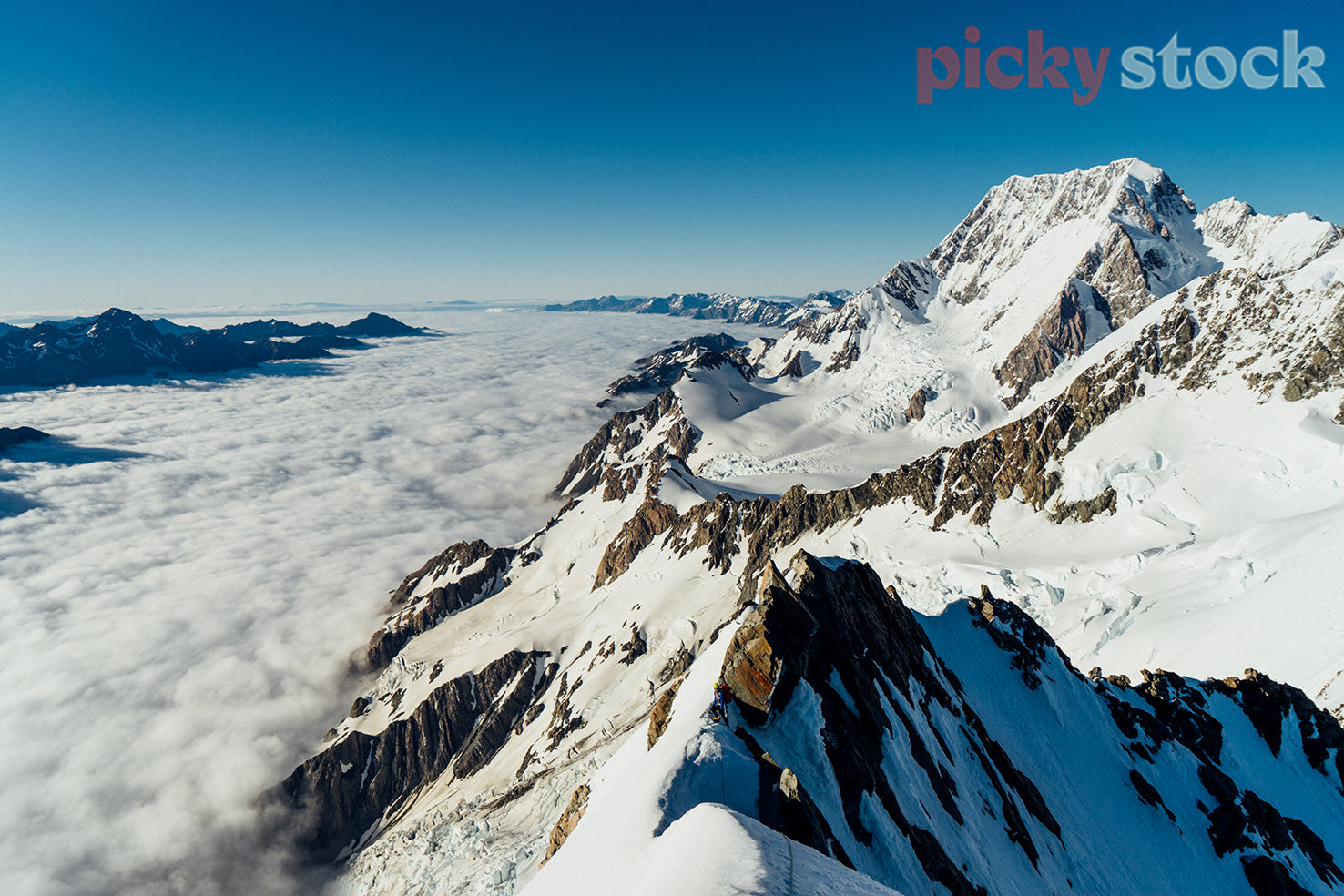 Mountain climber reaches the ridge above whitecapped mountain peaks and a sea of fog