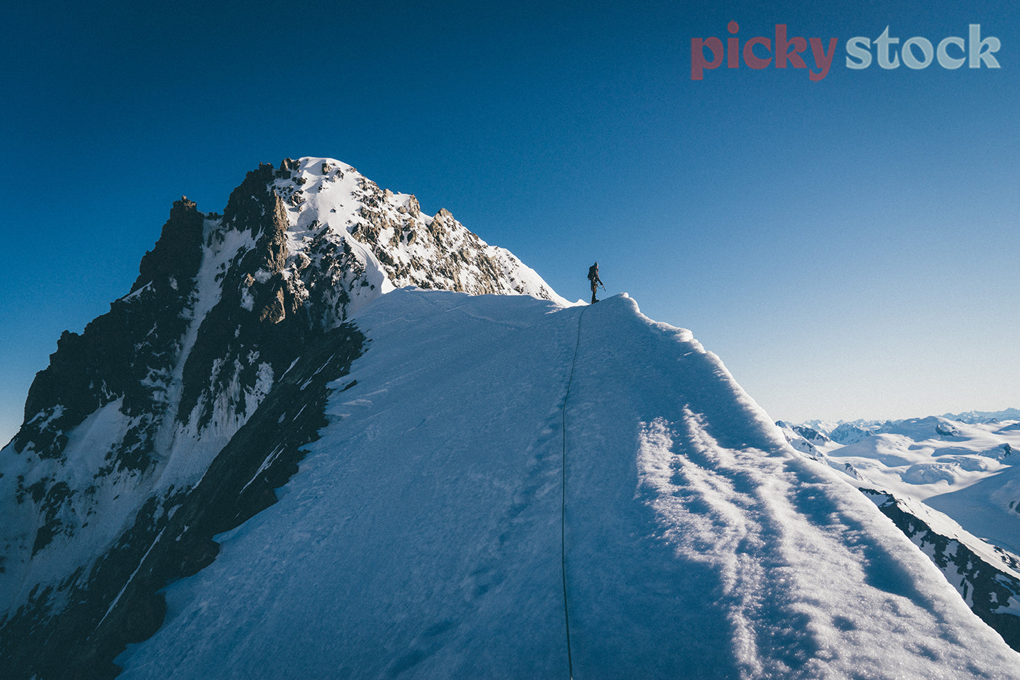 Mountain climber along an icy ridge overlooking the valley filled with clouds