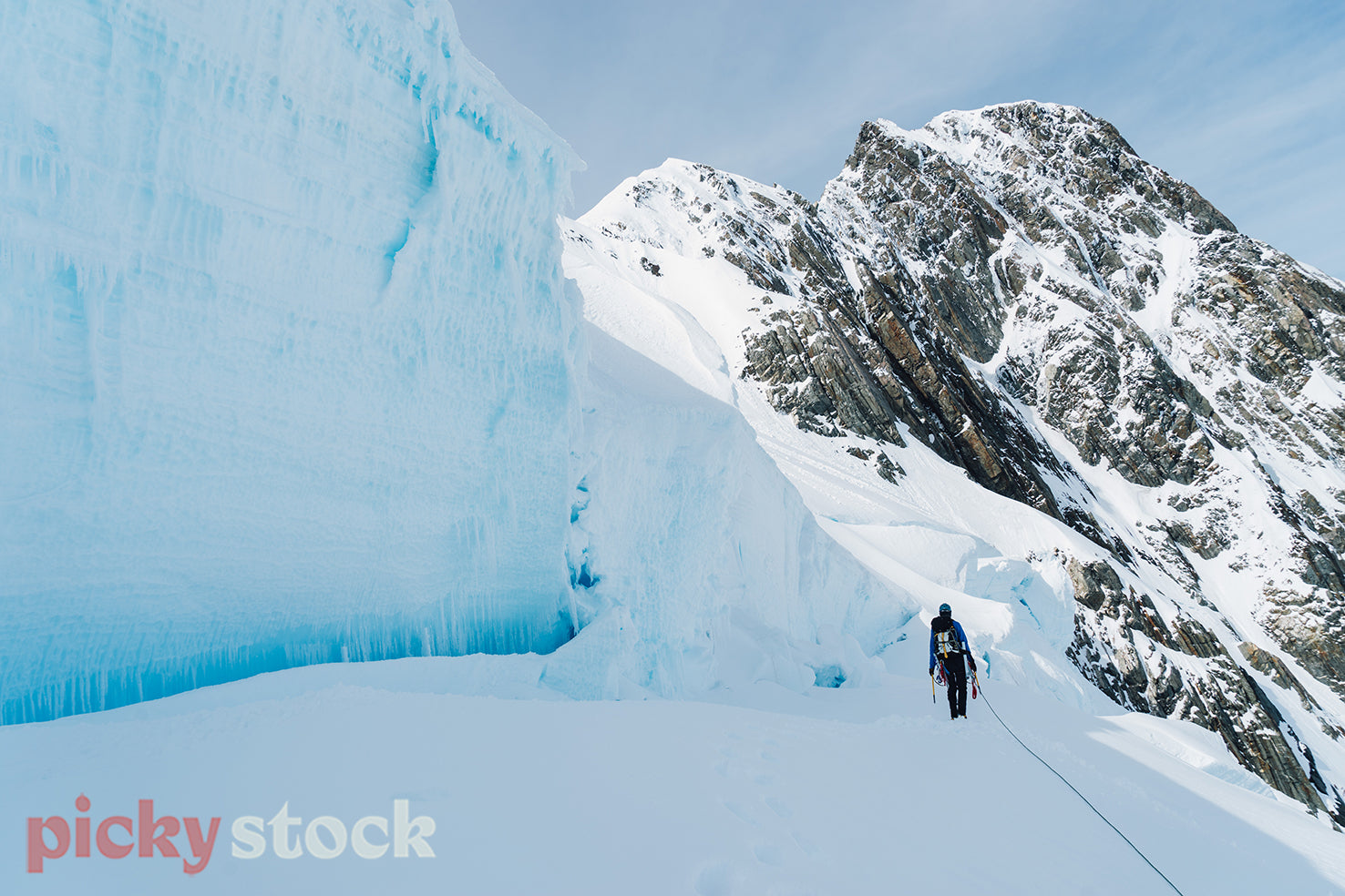 A mountain climber walks toward a snow bridge with the snow pack towering above on the side