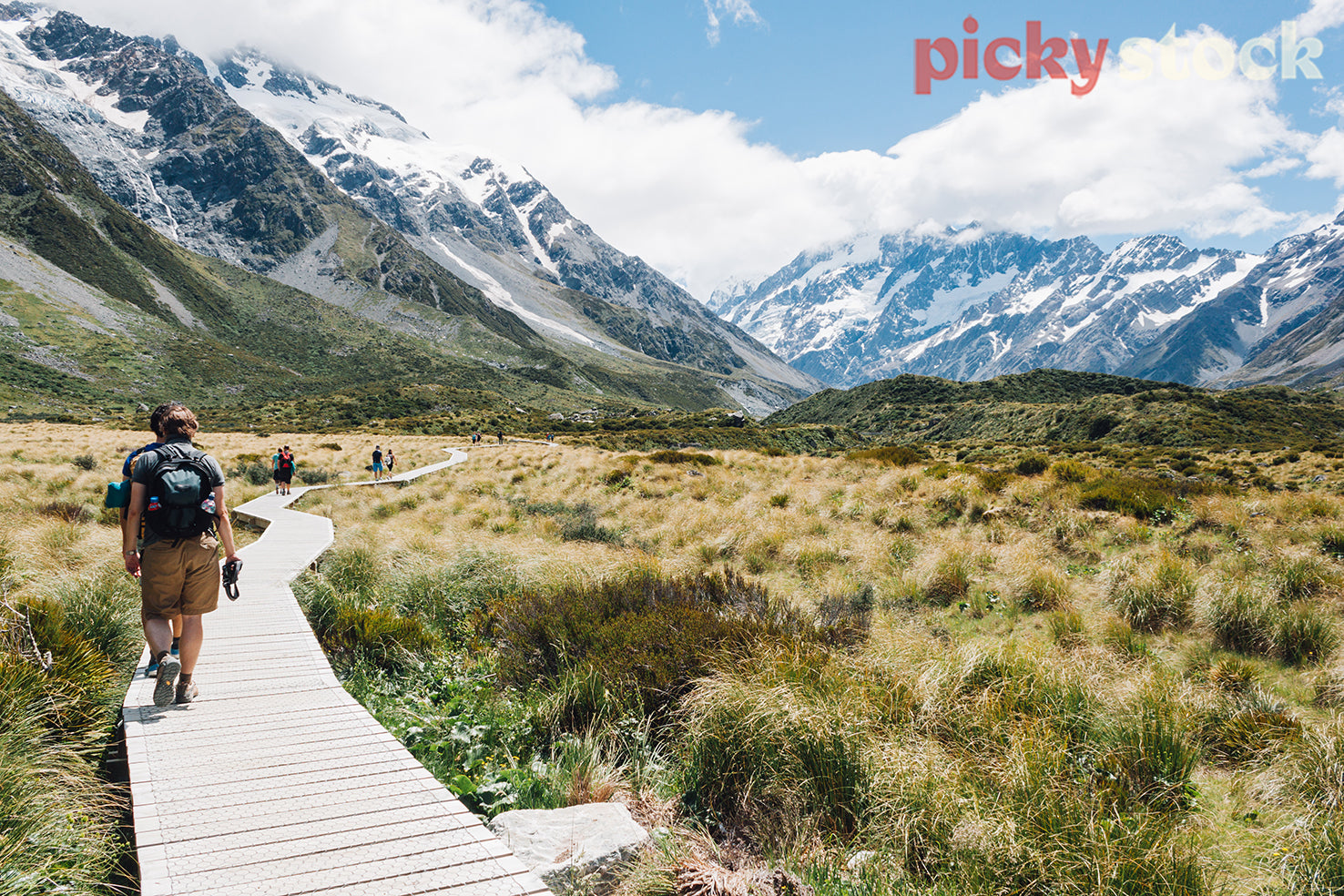 Trampers walk along a boardwalk, surrounded by snow capped mountains