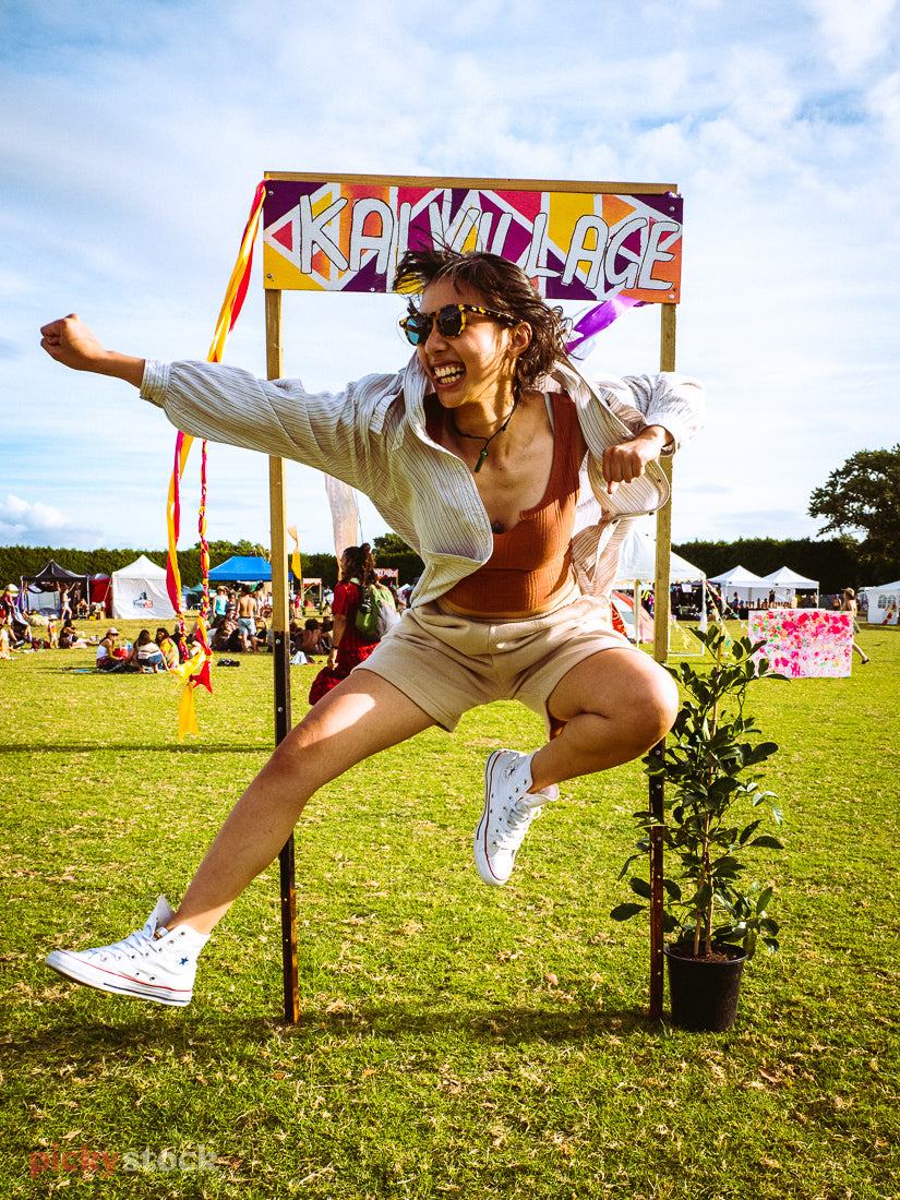 A young NZ-Asian lady jumps up high in a Kung-fu style pose, excited to be at a festival in Kumeū, Auckland. 