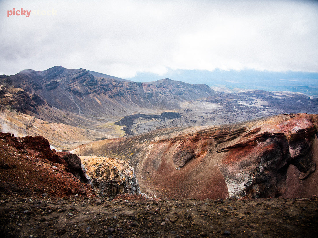 High angle image of Tongariro National Park, looking down from the ridge to the unearthed scoria. The earthy colours striking against the grey sky. 