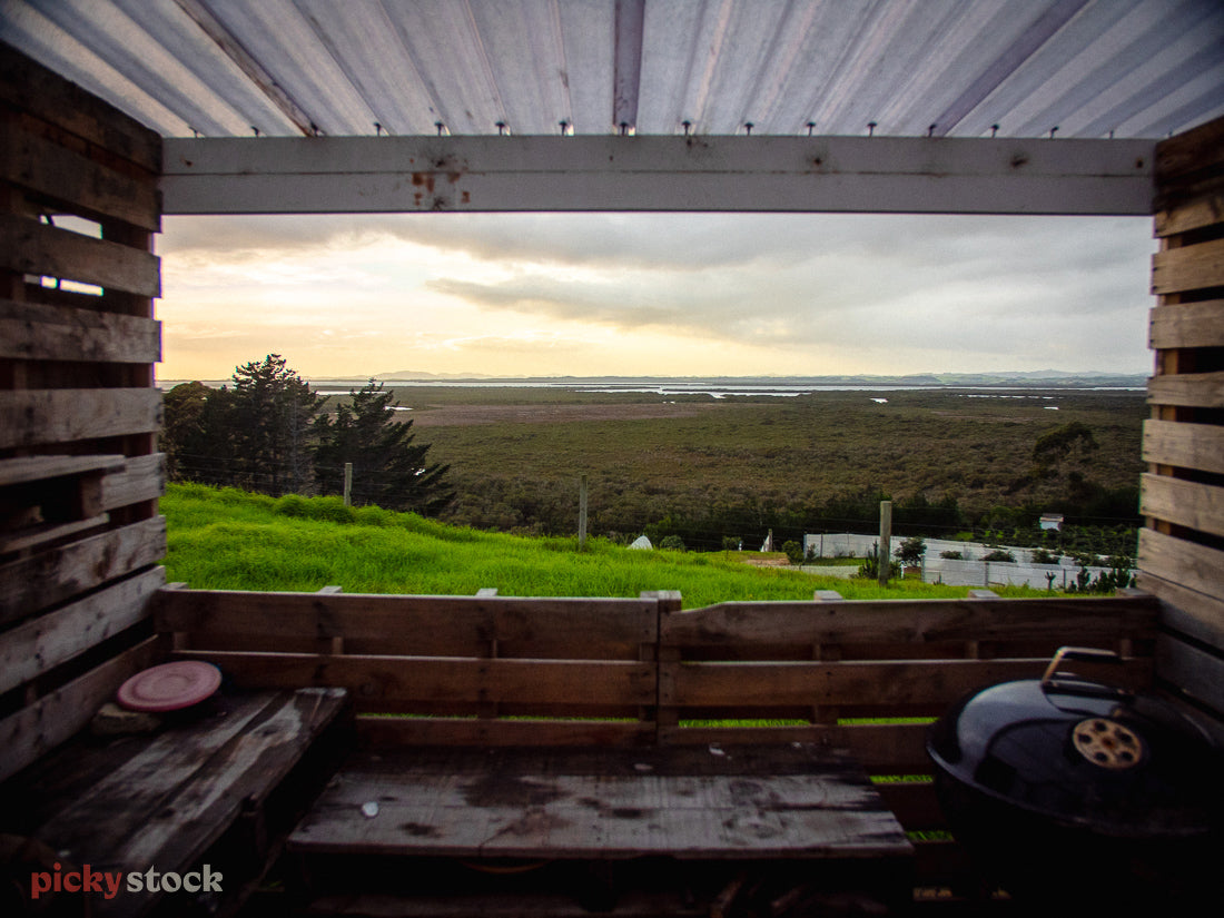 A landscape image looking out from under a covered deck out to the crops and scenery of Waiharara. The light has just come up for the day.