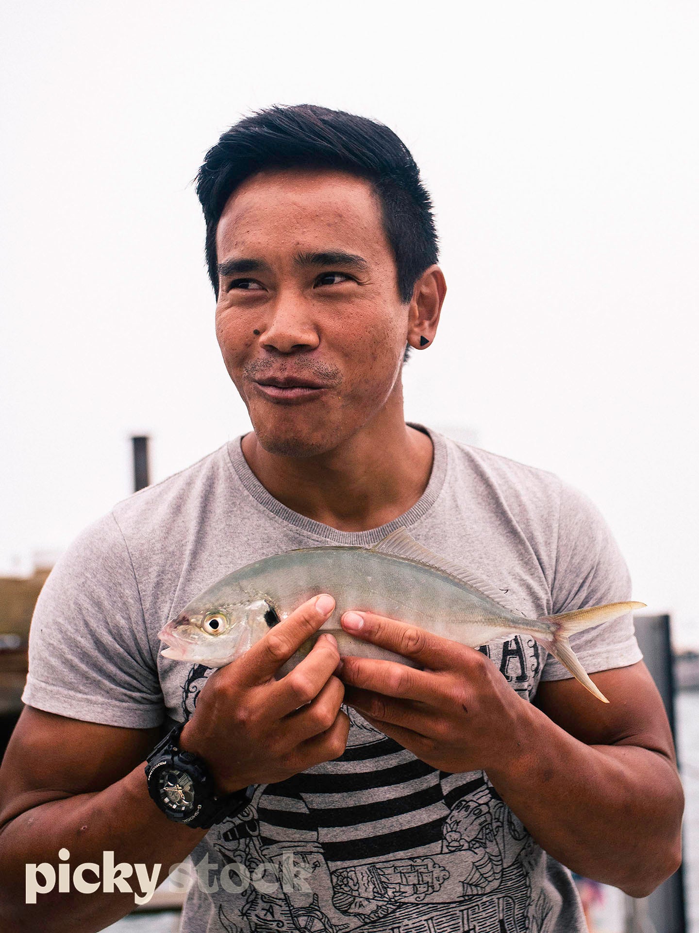 Portrait image of man holding a fish looking off camera. Fish middle of frame, front on to camera. 