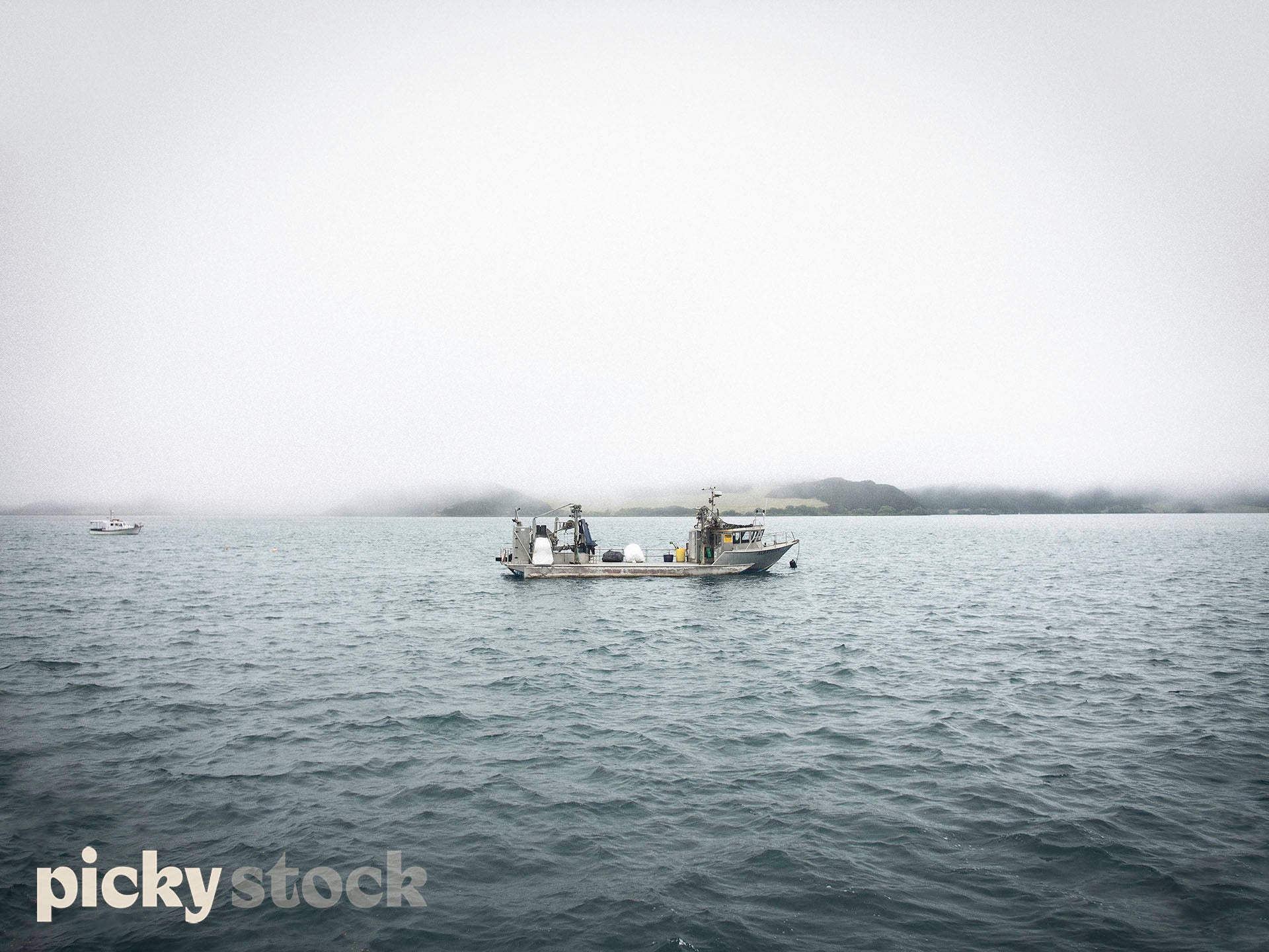 Fishing boat sitting in the middle of frame, small waves very misty day with low cloud. 
