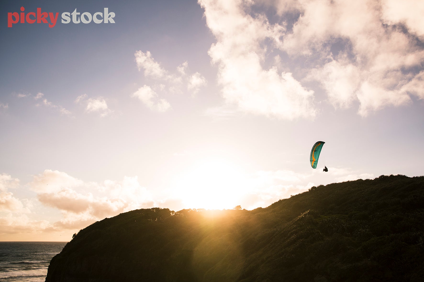 Paraglider over Muriwai beach with solar light flare.