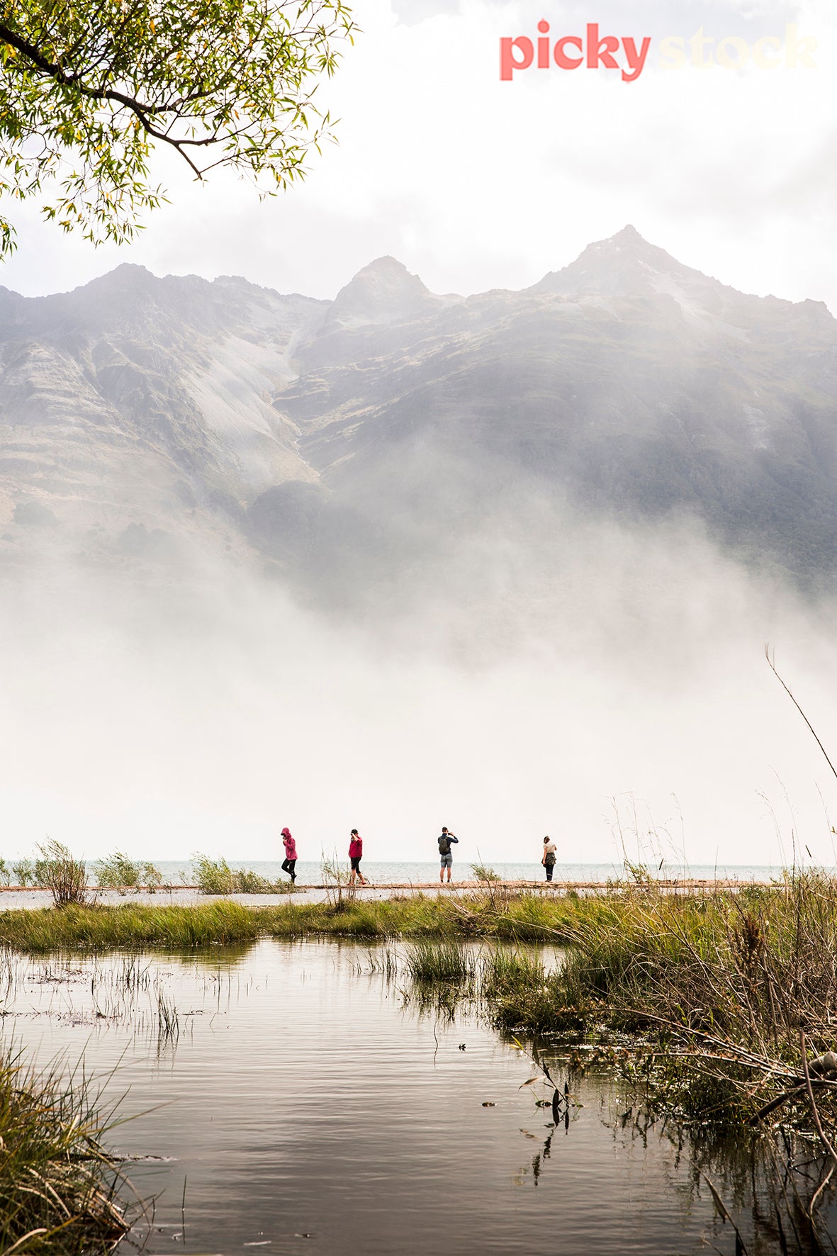People walking along the shores of Lake Wakatipu, against the fog. 