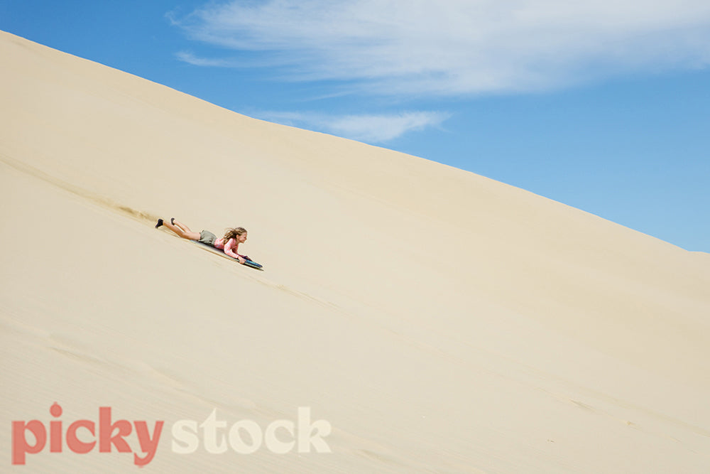 Girl on bodyboard sliding at speed down a sand dune