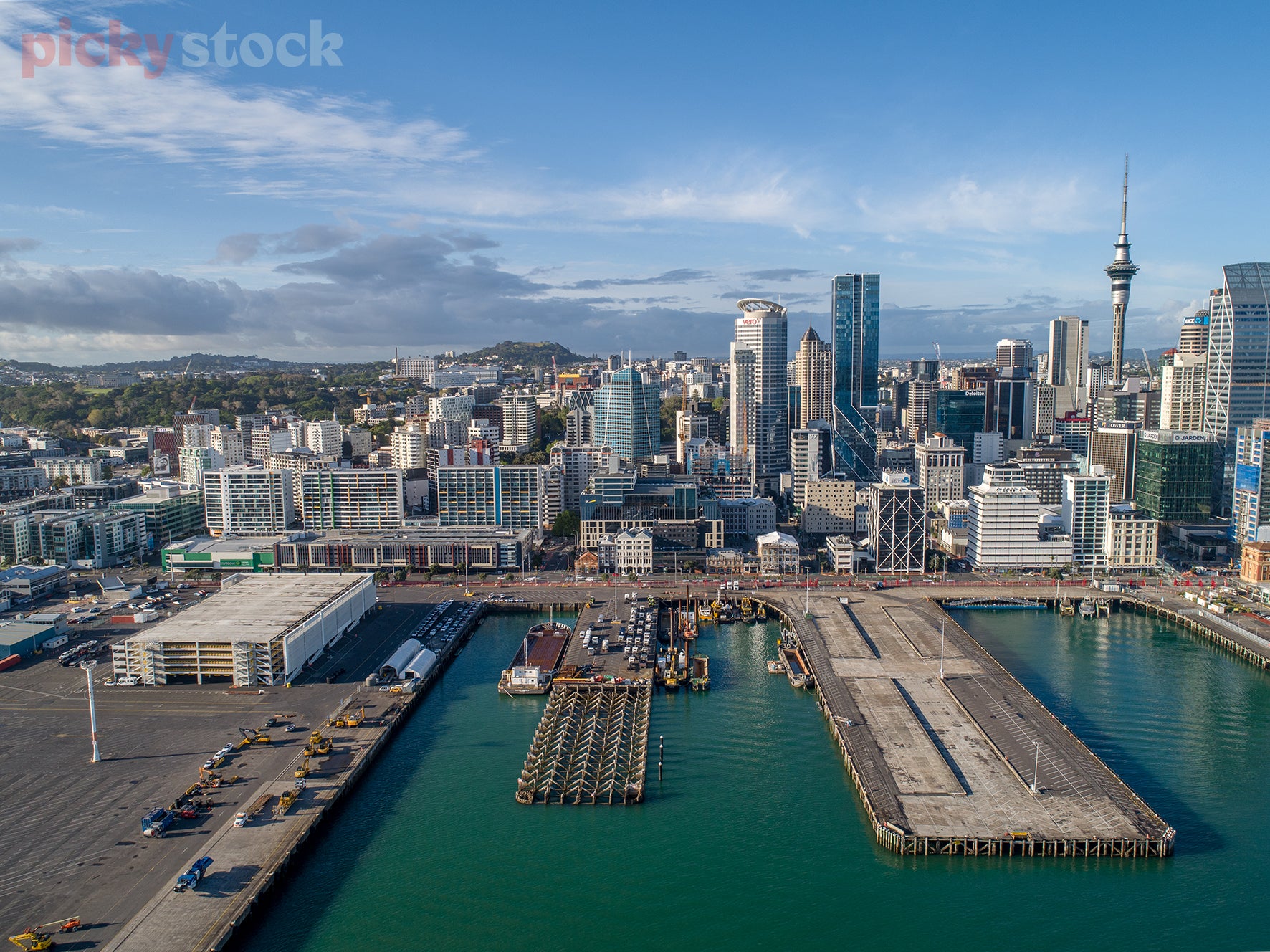 High angle image looking from Waitemata Harbour in along the ferry docks of Auckland City towards the big high rises and city scrapers. Blue sky and blue waters. 