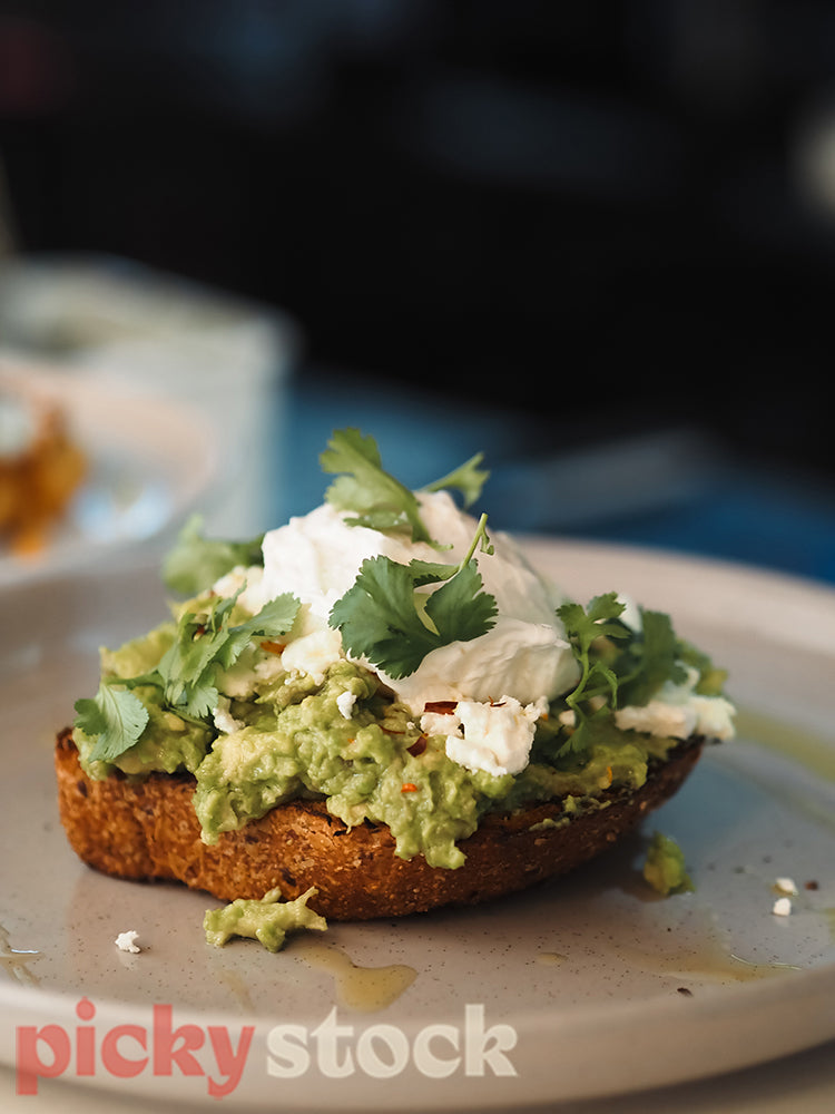 Avocado and feta toast with coriander and soft boiled egg served on a grey round plate.