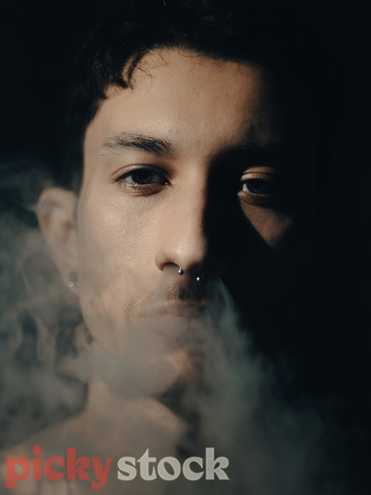 Portrait of a young adult man exhaling smoke.