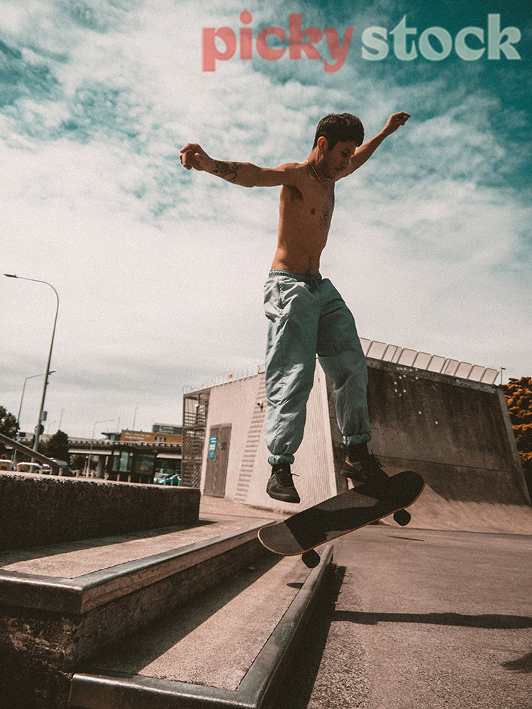 Shirtless young adult skater jumping over stairs.