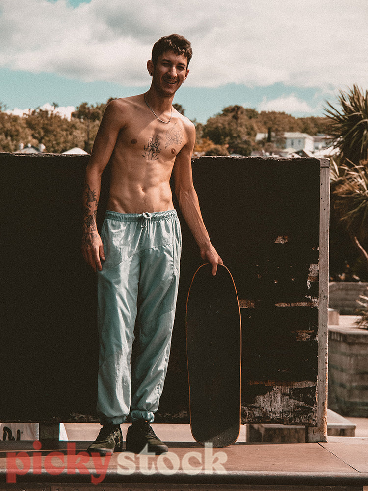 Shirtless young adult skater man on top of an half pipe.