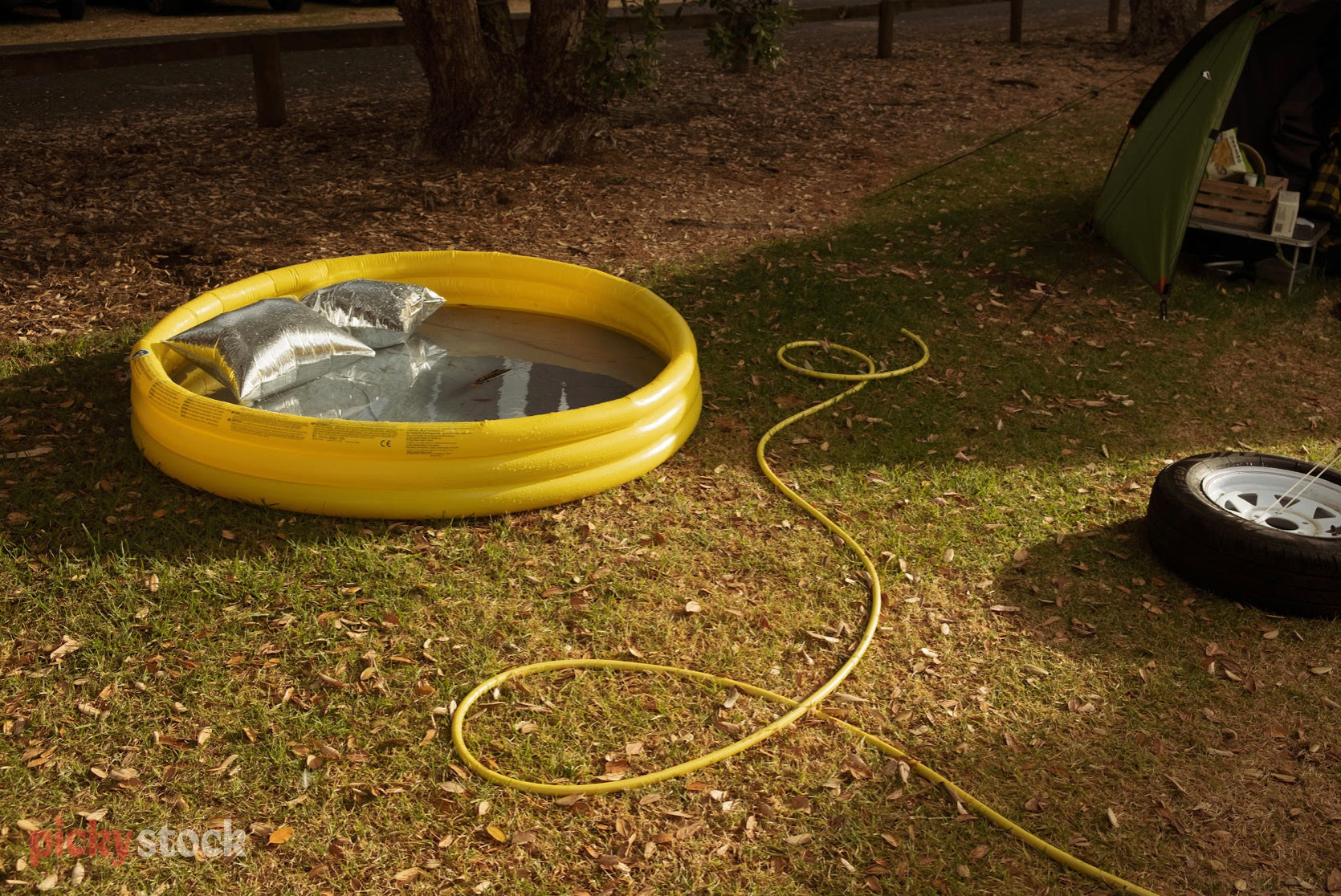 Outdoor bright yellow plastic blow-up paddling pool sits on yellow-tinted grass, with a yellow hose spiralling through the frame. 