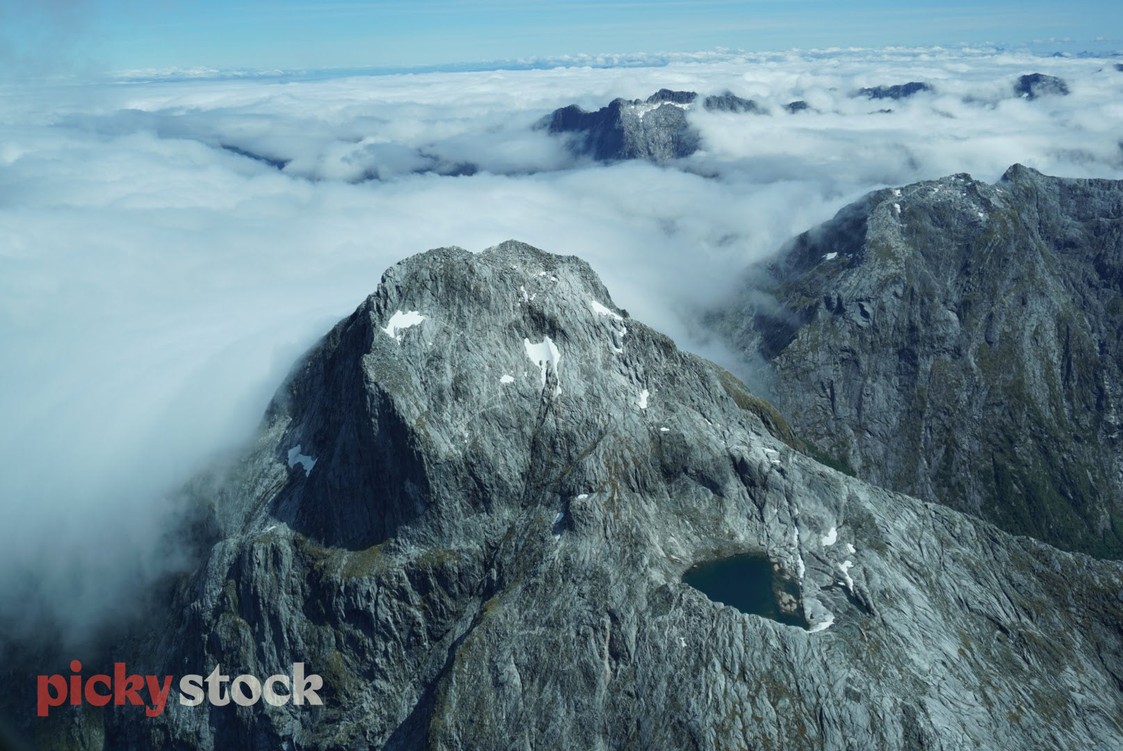 A New Zealand mountain top seen from cloud level, the misty clouds roll in between the grey, sheer, mountain peaks. 
