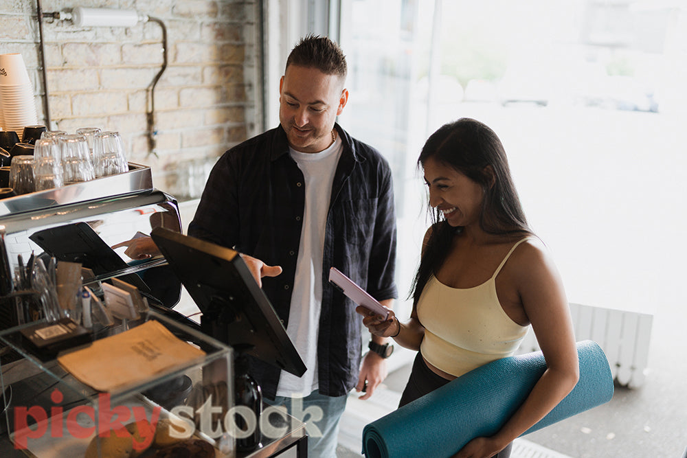 Woman and man ordering meal at counter on an ipad at cafe. Lady holding blue yoga mat.