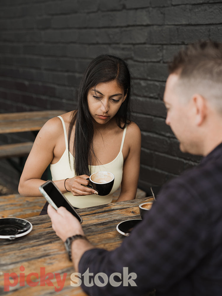 Indian woman looks at white mans phone in a cafe.