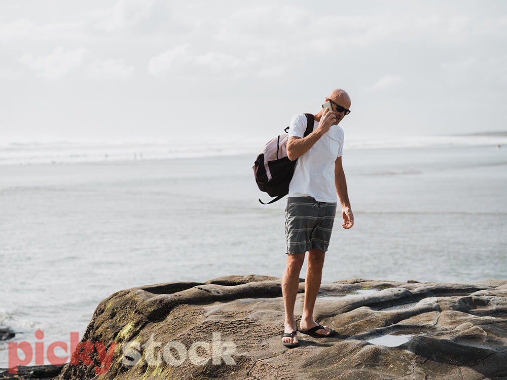 Man standing on rock by ocean talking on mobile phone