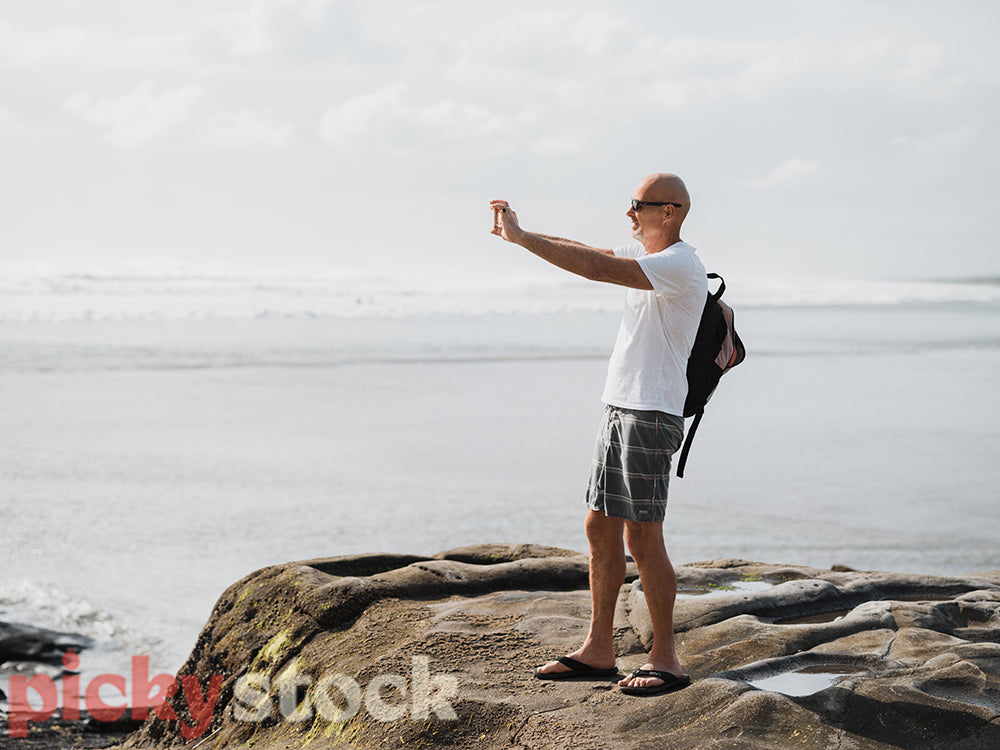 Man standing on rocks taking photo of ocean