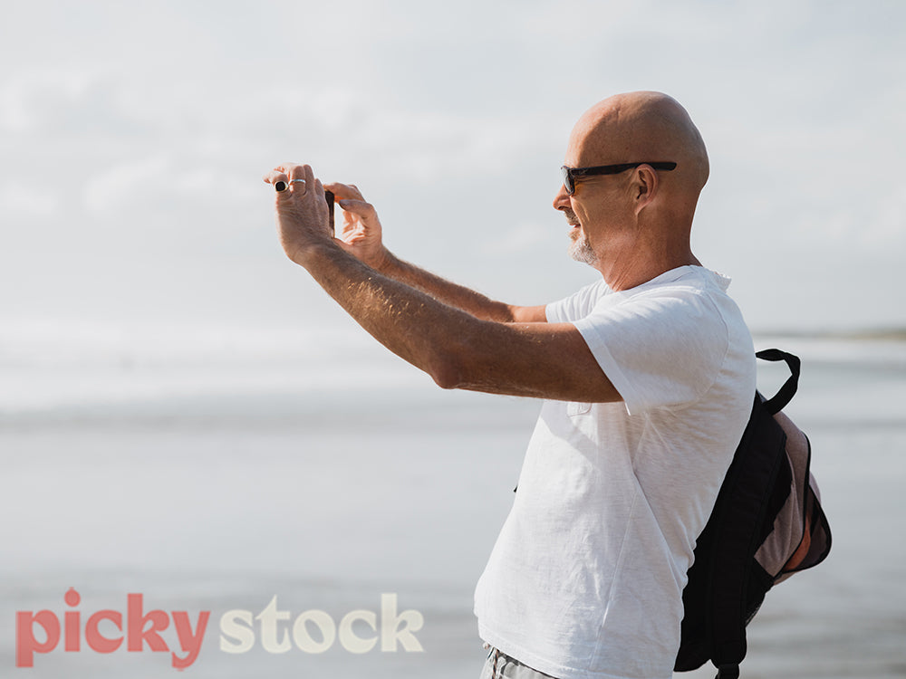 Man standing on rocks taking photo of ocean