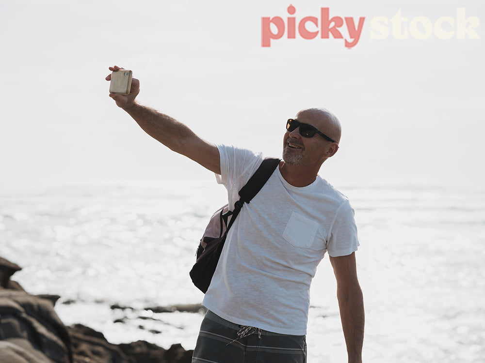 Man standing on rocks taking selfie with ocean