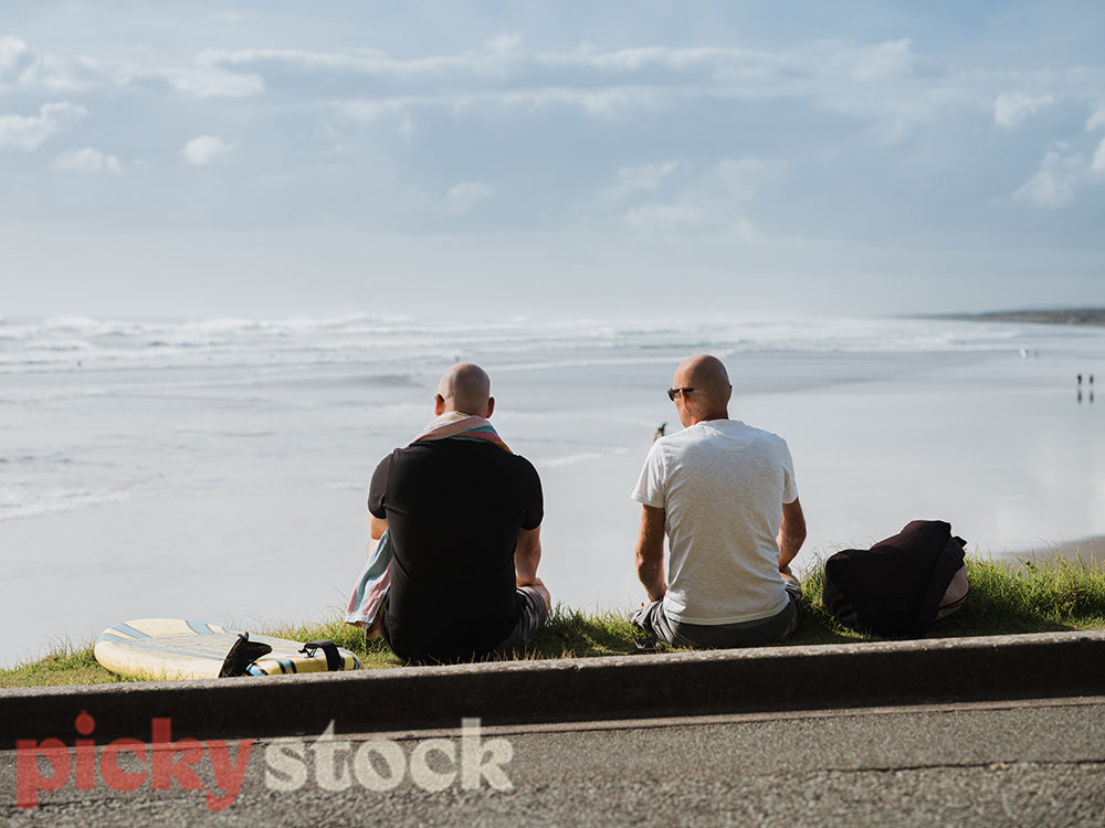 Two men sitting on grass looking out at ocean