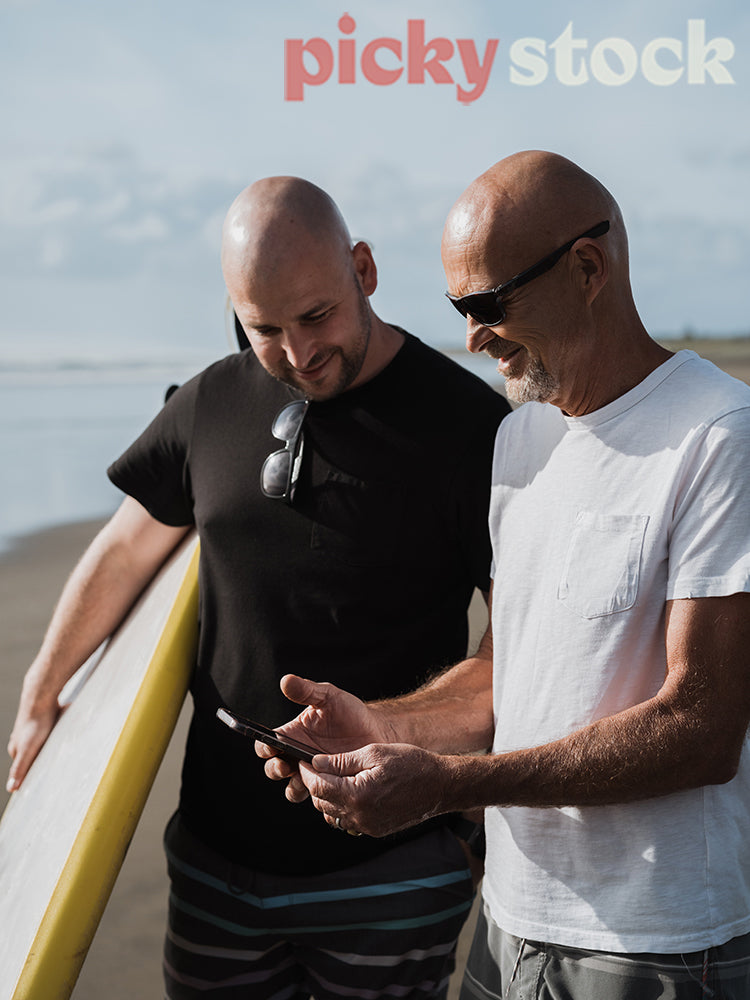 Two man by ocean, looking down at mobile phone