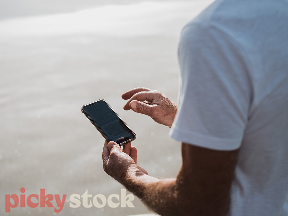 Crop image of mans hands holding mobile device. Sand in background