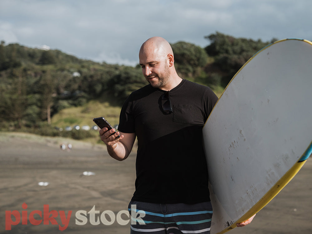 Man standing at beaxch with surf board on mobile phone