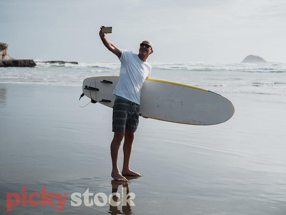 Man standing at waters edge by ocean taking selfie