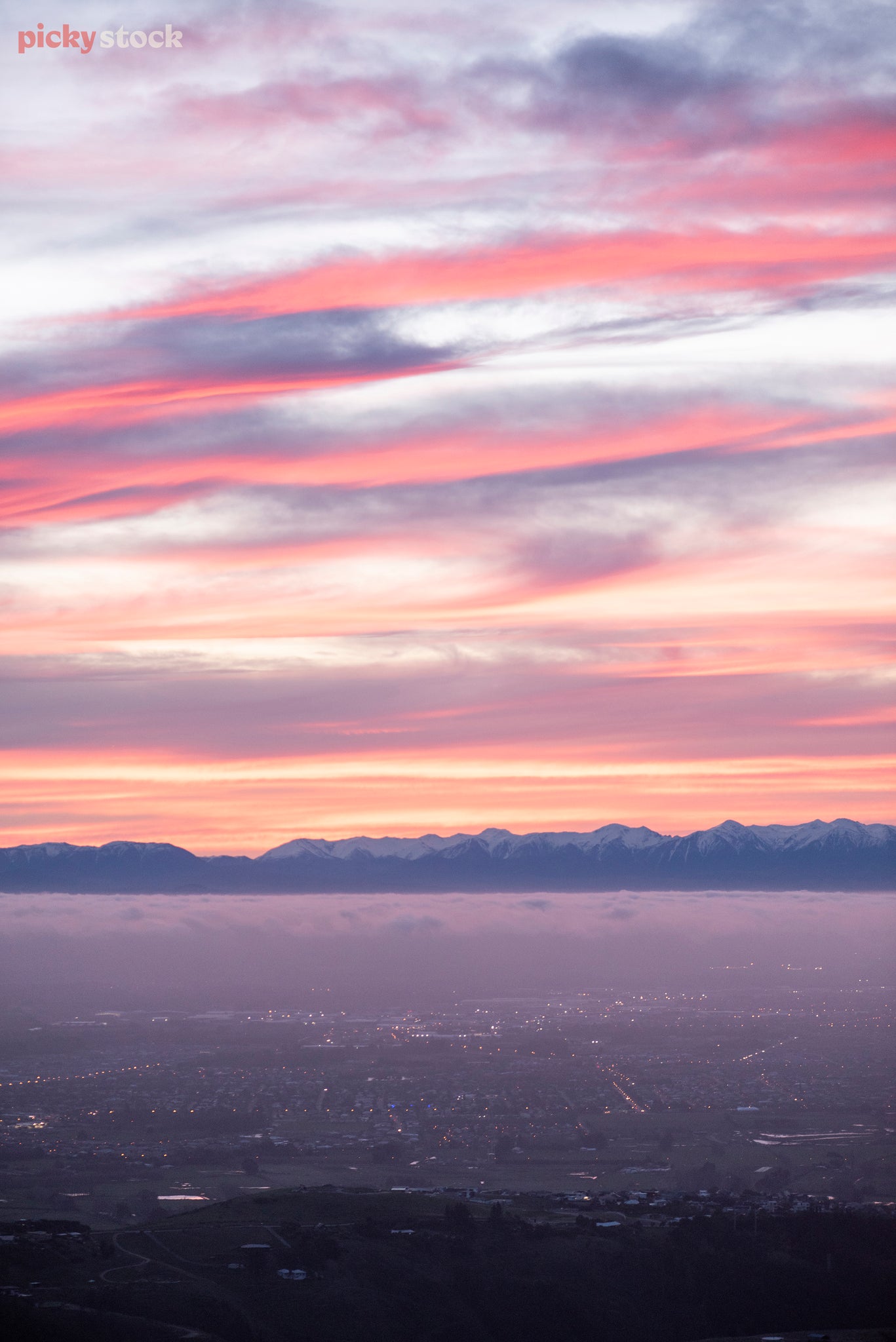 View of Christchurch from the Port Hills as the smog and early evening light hit. The sky and clouds are vivid pink, blue and lilac creating a dramatic feeling. 