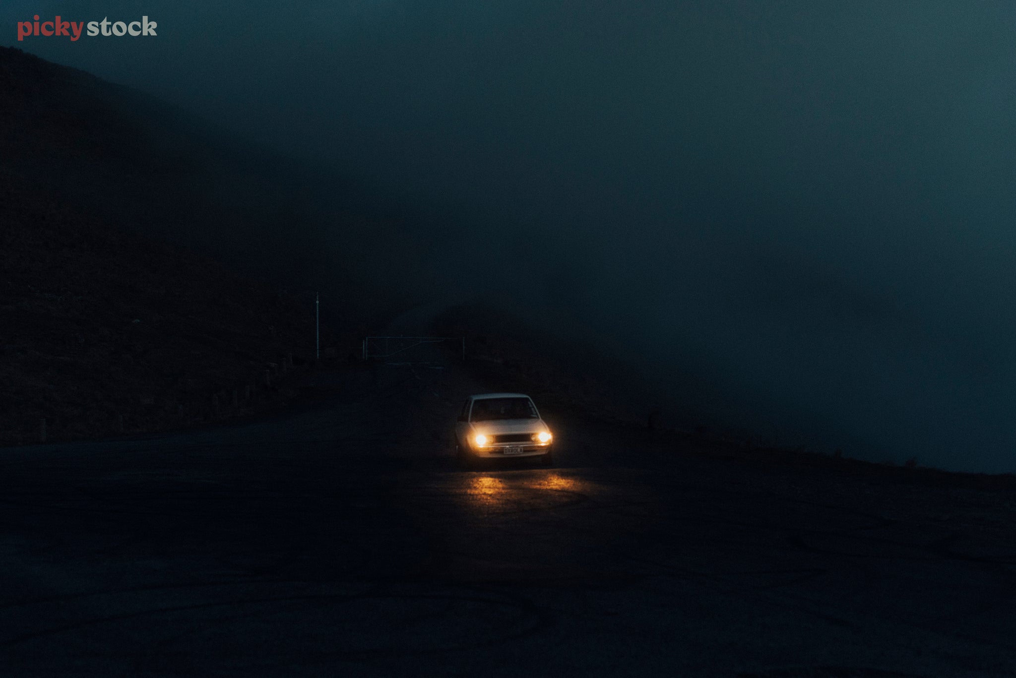 A dark shot of a white VW polo car driving towards the camera on a dark day. 